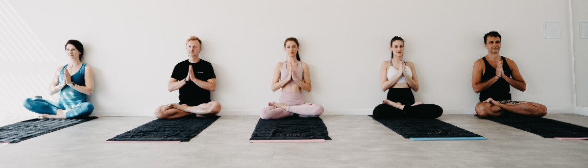 Skupina cvičenců v meditaci vsedě ve světlém jógovém sále